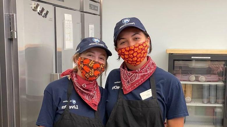 Two women, wearing masks and hats, pose for a photo at work.