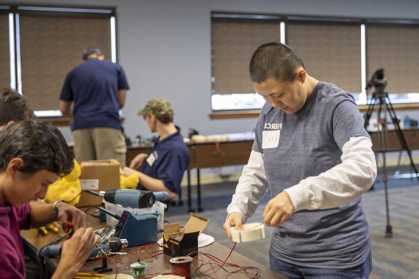 博克斯 student helps high school student with soldering toys.